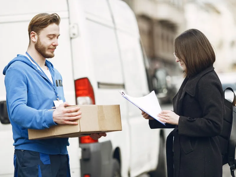 Courier handing a parcel to a customer beside a van